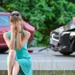 Stressed woman driver sitting on street side shocked after car accident. Road safety and insurance